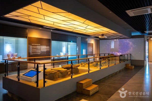 불 밝힌 천장 아래 돌 유구를 재현한 전시대와 진열장