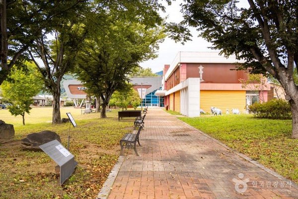 나무 그늘 아래 벤치가 놓인 벽돌 산책길과 건물